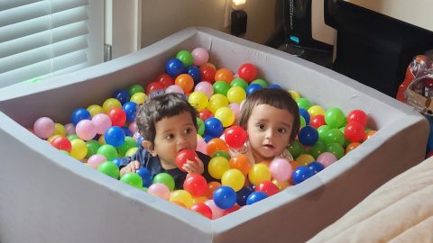 Twin toddlers in a small ball pit looking up at the camera.
