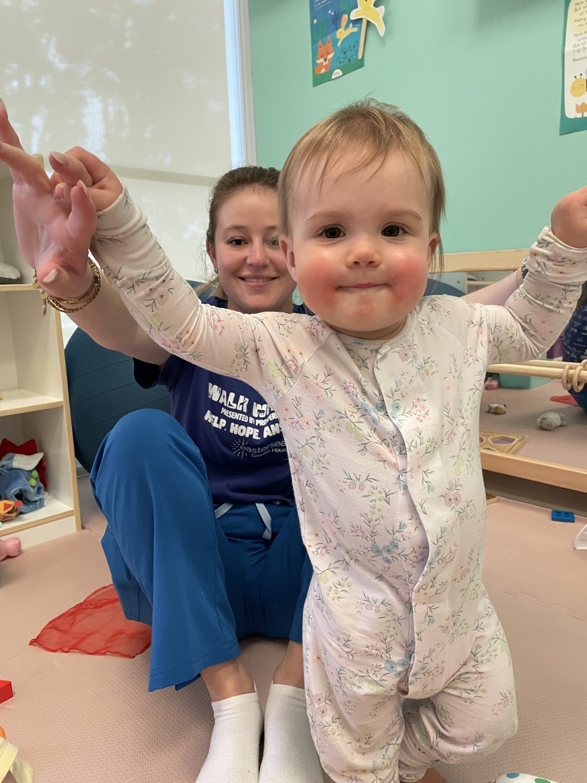 A baby standing with help from teacher.
