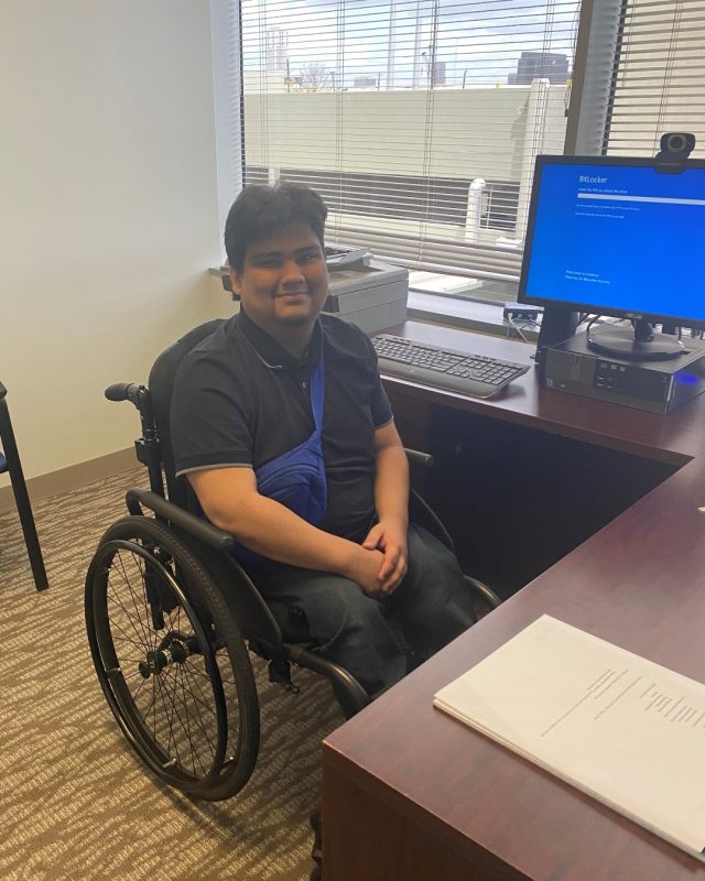 Man in a wheelchair at a corner desk with a computer.