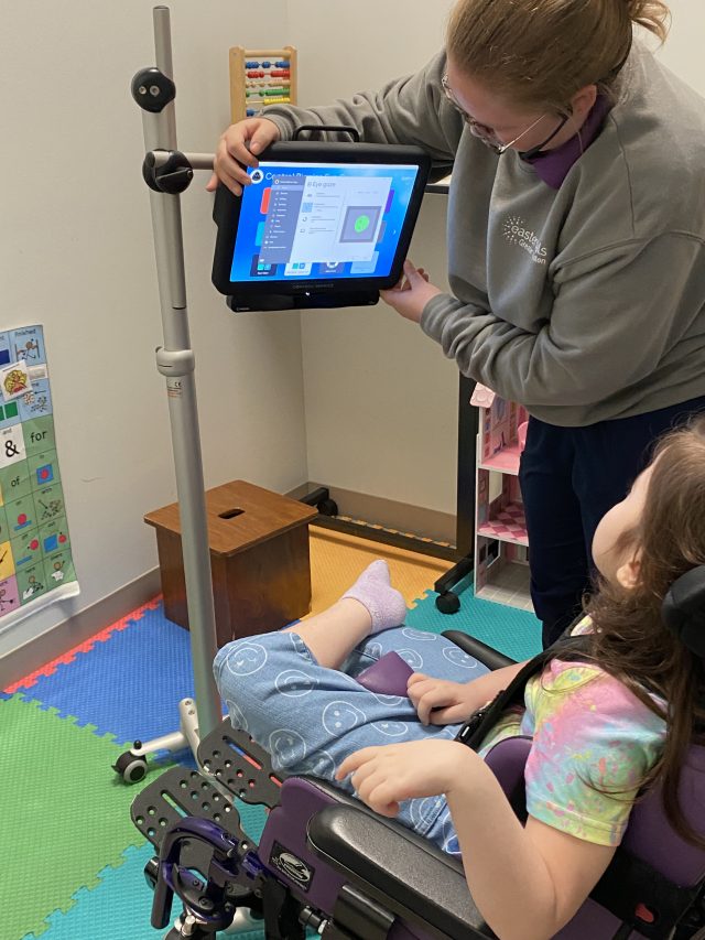 Speech Language Pathologist Daryn supporting Violet as she practices using an Eyegaze device.